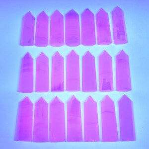 May include: Twenty-four pink crystal points arranged in three rows of eight. The points are all the same size and shape, and they are all pointed at the top.