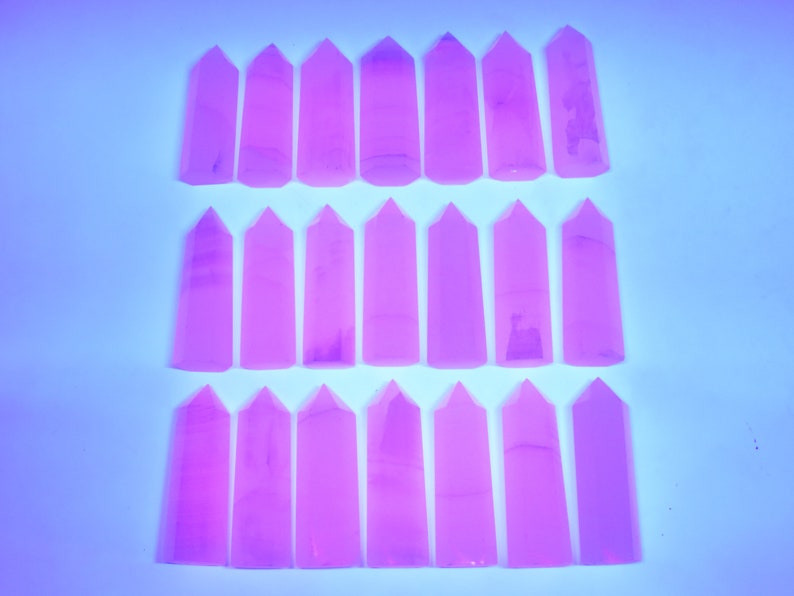 May include: Twenty-four pink crystal points arranged in three rows of eight. The points are all the same size and shape, and they are all pointed at the top.