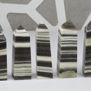 May include: Five black and white striped crystal points, also known as banded agate, arranged in a row on a white surface.
