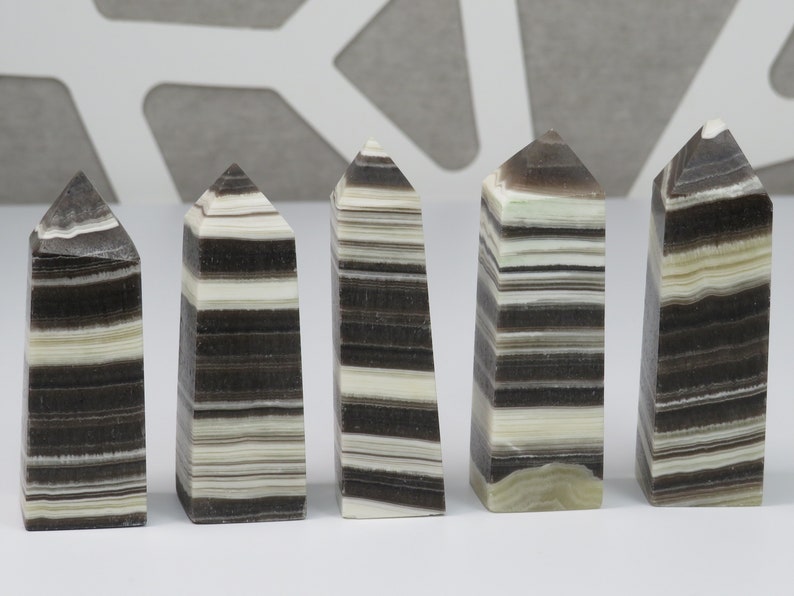 May include: Five black and white striped crystal points, also known as banded agate, arranged in a row on a white surface.