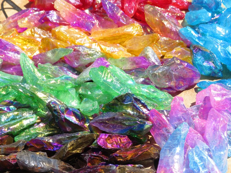 May include: A collection of iridescent crystal points in various colours, including red, orange, yellow, green, blue, and purple. The crystals are arranged in a rainbow pattern.