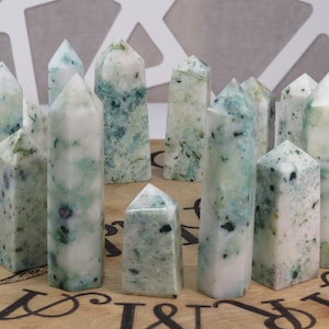 May include: A collection of white and green crystal points, also known as green apophyllite, arranged in a circle on a wooden surface.