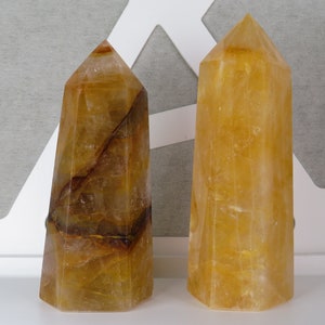 May include: Two yellow citrine crystal points, one with brown inclusions, on a white surface.