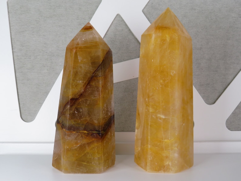 May include: Two yellow citrine crystal points, one with brown inclusions, on a white surface.