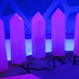 May include: Six pink crystal points arranged in a row on a wooden surface. The crystals are illuminated by a blue light, causing them to glow.