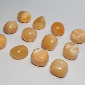 May include: A collection of twelve tumbled orange calcite stones. The stones are smooth and polished, with a variety of shades of orange and white.