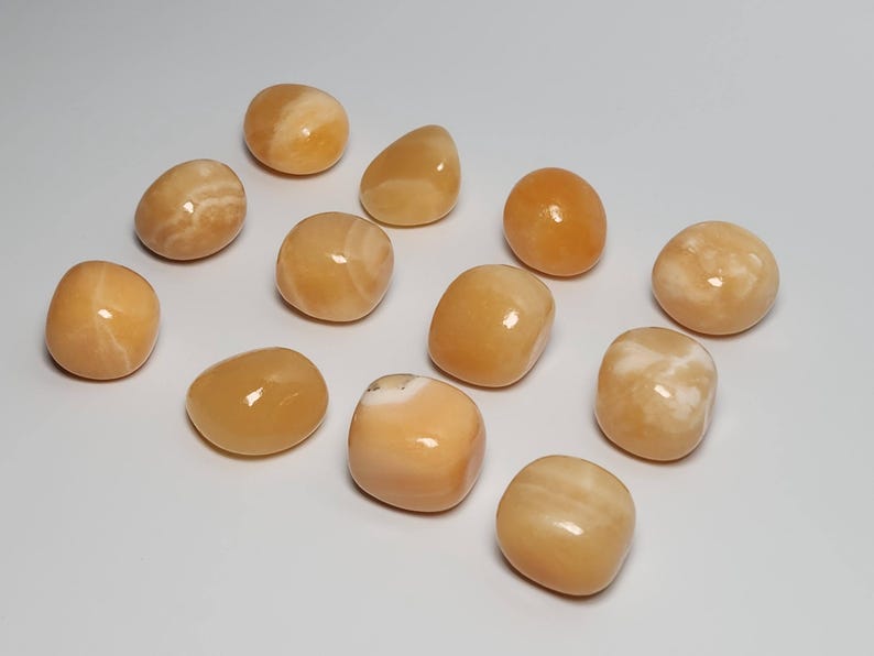 May include: A collection of twelve tumbled orange calcite stones. The stones are smooth and polished, with a variety of shades of orange and white.