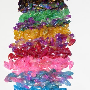 May include: A rainbow assortment of iridescent crystal points. The crystals are arranged in a vertical stack, with the colours transitioning from purple to blue, pink, red, yellow, green, and finally purple.