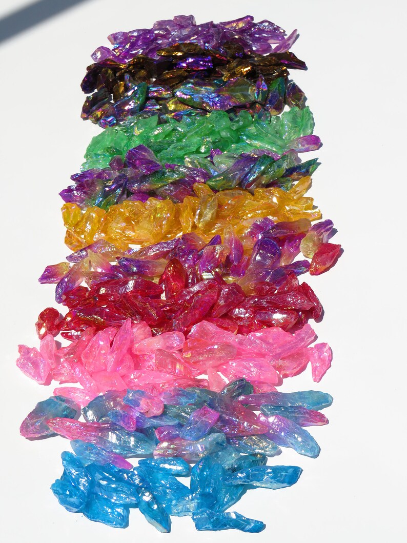 May include: A rainbow assortment of iridescent crystal points. The crystals are arranged in a vertical stack, with the colours transitioning from purple to blue, pink, red, yellow, green, and finally purple.