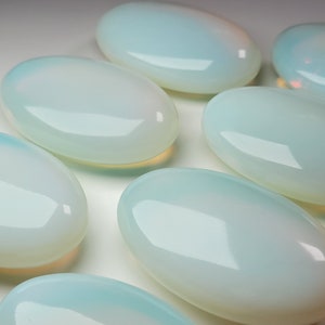 May include: Seven smooth, oval-shaped, polished opal stones in various shades of white and light blue.