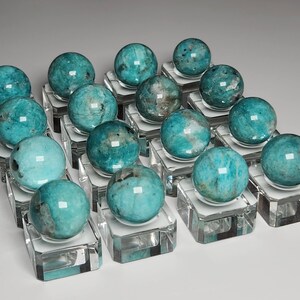May include: A collection of 18 teal green gemstone spheres displayed on clear acrylic stands. The spheres are polished and have a smooth, glassy finish.