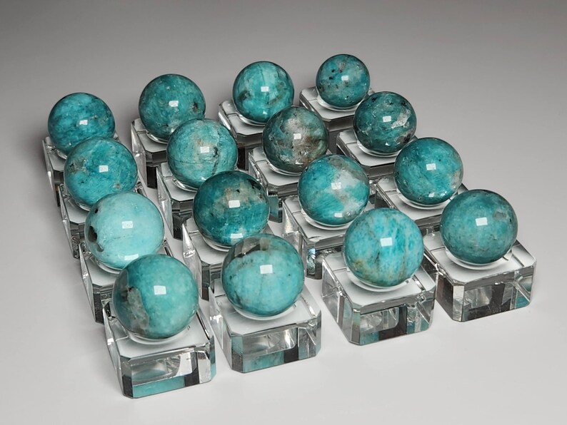 May include: A collection of 18 teal green gemstone spheres displayed on clear acrylic stands. The spheres are polished and have a smooth, glassy finish.