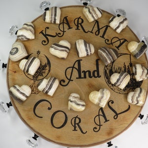 May include: A wooden round tray with the words "Karma And Coral" engraved on it. The tray is decorated with 15 heart-shaped striped onyx stones.