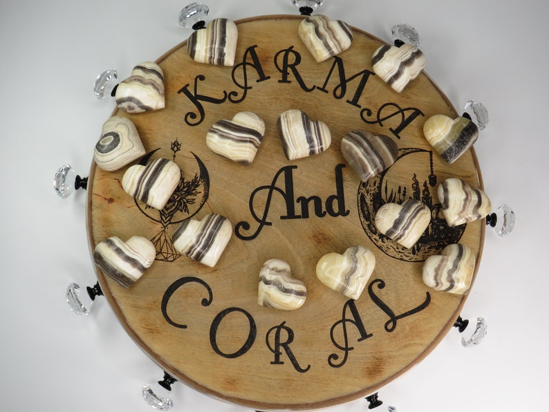 May include: A wooden round tray with the words "Karma And Coral" engraved on it. The tray is decorated with 15 heart-shaped striped onyx stones.