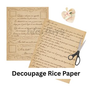 May include: Two sheets of tan rice paper featuring vintage-style cursive French handwriting and decorative flourishes. One sheet includes rectangular borders, while the other is filled with text. A small heart-shaped floral embellishment and black scissors.