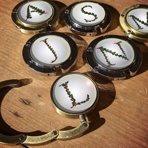 Puede incluir: Seis clips de bolso de metal dorado con fondo blanco y follaje verde formando las letras "CLASSM".