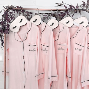 Five pink custom sleep shirts with a blush eyelash sleep mask attached to the hangers.