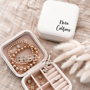 Travel-sized jewelry box opened with a pink velvet interior filled with small jewelry pieces.