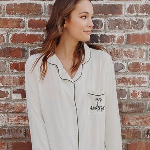 Woman leaning against a brink wall wearing a white shirt