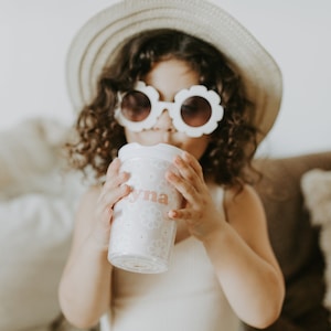 Little girl wearing a hat and flower shape sunglasses holding a flower girl cup