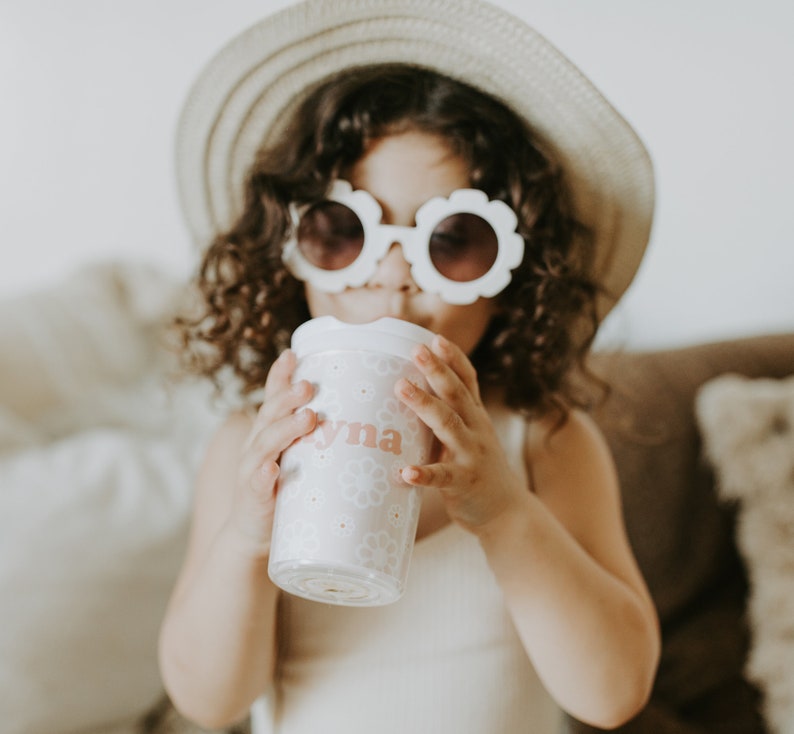 Little girl wearing a hat and flower shape sunglasses holding a flower girl cup