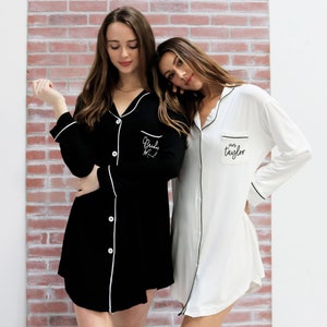 Two girls wearing a black and a white sleep shirt against a light brink wall
