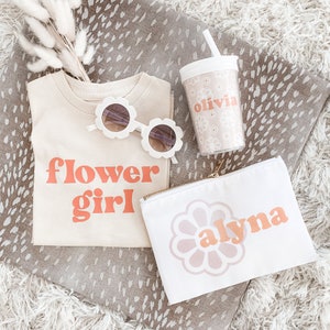 Flower girl shirt, olivia cup and alyna cosmetic bag laying on a grey blanket