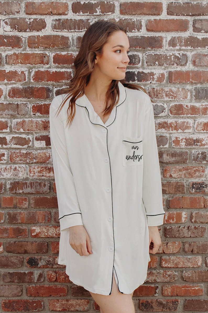 Woman leaning against a brink wall wearing a white shirt