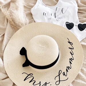 Tan sun hat with black vinyl text and black bow around crown of hat
