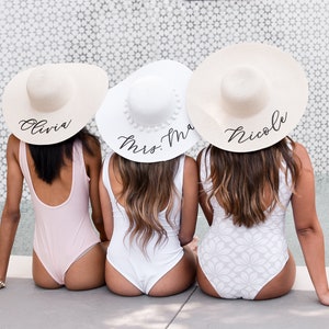 Tan sun hat with black vinyl text, white sun hat with white pom poms around crown with black vinyl text, tan sun hat with black vinyl text.