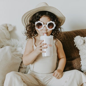 Little girl wearing a hat and flower shape sunglasses holding a flower girl cup