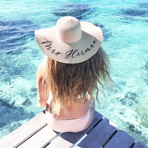 girl wearing tan sun hat with black vinyl text  sitting by the ocean