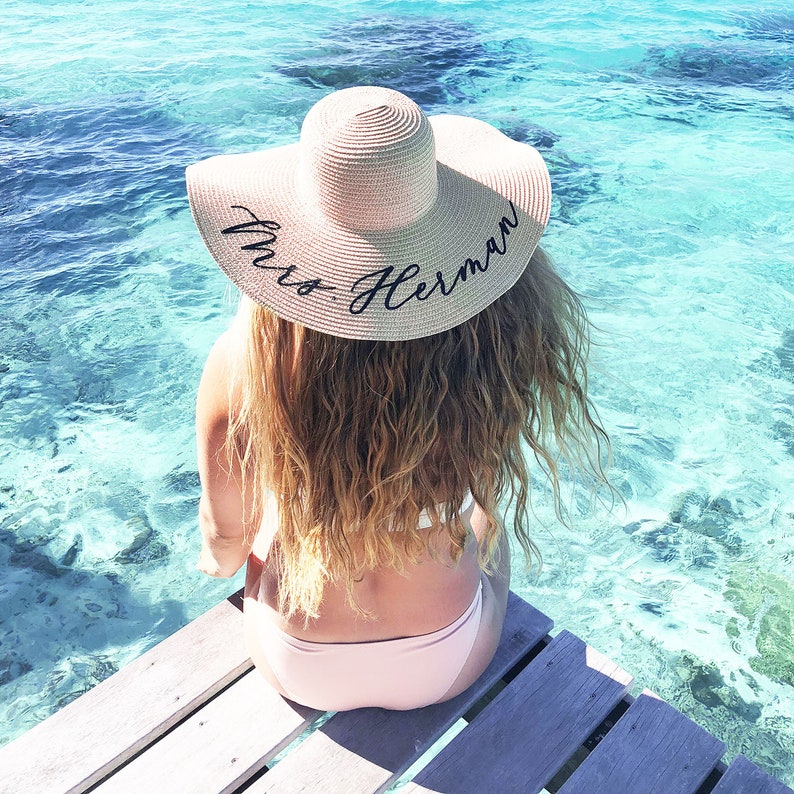 girl wearing tan sun hat with black vinyl text  sitting by the ocean