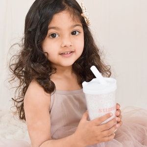 Little girl with brown hair and tulle dress holding a flower girl cup