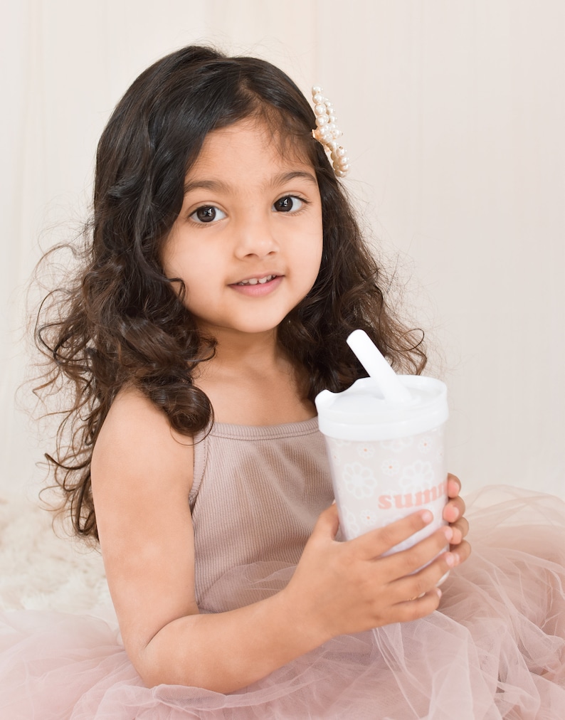 Little girl with brown hair and tulle dress holding a flower girl cup