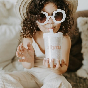 Little girl wearing a hat and flower shape sunglasses holding a flower girl cup