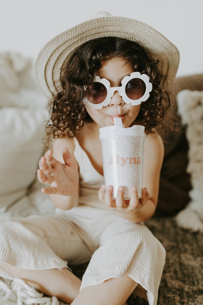 Little girl wearing a hat and flower shape sunglasses holding a flower girl cup