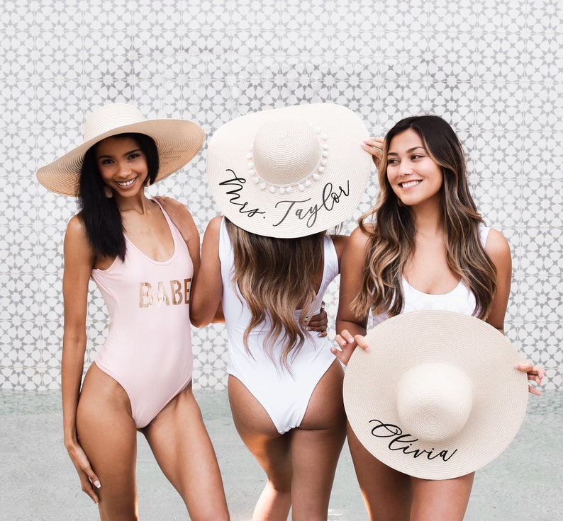 3 tan sun hats with black vinyl text. Middle sun hat with white pom poms surrounding crown