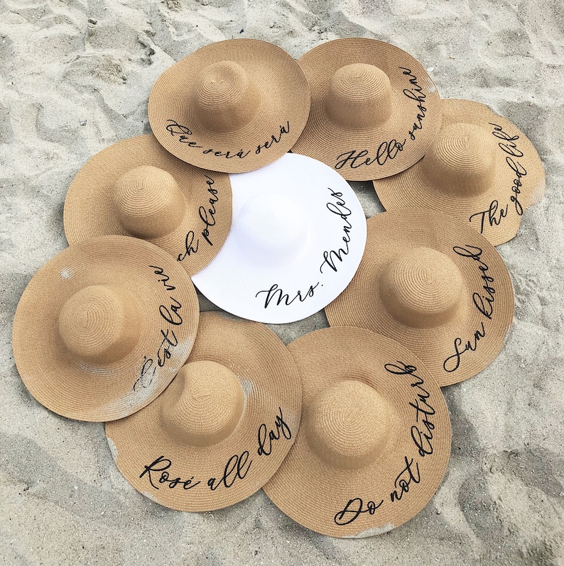 8 tan sun hats with black vinyl text surrounding white sun hat with black vinyl text