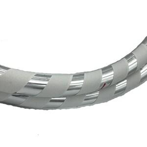 K&ouml;nnte beinhalten: Ein wei&szlig;er und silberner Reifen mit einer strukturierten Oberfl&auml;che. Der Reifen besteht aus zwei Rohrst&uuml;cken, die mit wei&szlig;em Klebeband und silbernem reflektierendem Klebeband umwickelt sind.