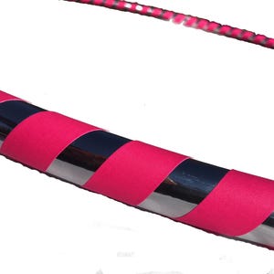 May include: A pink and silver exercise hoop with a striped pattern. The hoop is made of metal and has a padded covering.