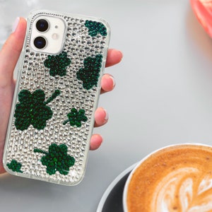 May include: A clear phone case with a sparkly silver background and green shamrock designs. The case is designed for an iPhone.