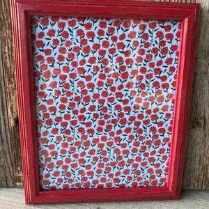 May include: A red wooden picture frame with a white background and a red floral pattern. The frame has a distressed look.
