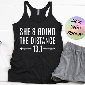 May include: Black tank top with white text that reads "She's going the distance 13.1" with arrows on either side of the number.