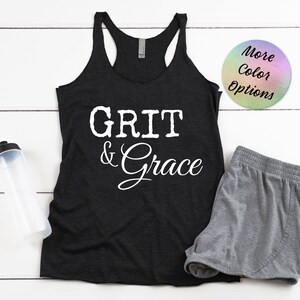 May include: Black tank top with the text "GRIT & Grace" in white lettering. The tank top is on a white wooden surface with a water bottle and gray shorts.