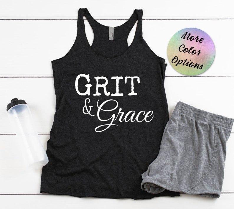 May include: Black tank top with the text "GRIT & Grace" in white lettering. The tank top is on a white wooden surface with a water bottle and gray shorts.