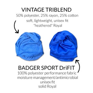 Op de afbeelding: Twee gevouwen T-shirts, een blauwe en een hemelsblauwe. Het blauwe T-shirt is gelabeld "BADGER SPORT DriFIT 100% polyester performance fabric moisture management/antimicrobial unisex fit solid Royal". Het hemelsblauwe T-shirt is gelabeld "VINTAGE TRIBLEND 50% polyester, 25% rayon, 25% katoen zacht, lichtgewicht, unisex fit "heathered" Royal"