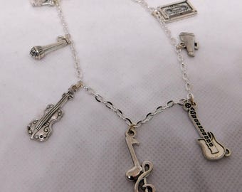 May include: Silver-toned charm bracelet featuring musical instrument charms. The bracelet includes charms of a violin, microphone, guitar, treble clef, cassette tape, and a megaphone. The bracelet is displayed on a white surface.