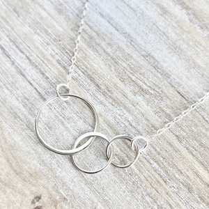 May include: A silver necklace with four interlocking circles. The circles are of different sizes and are connected to a delicate silver chain.