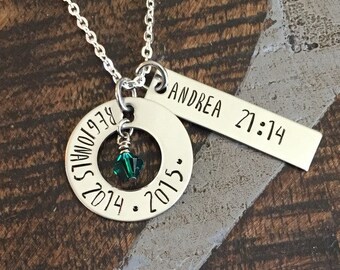 May include: Silver necklace with a round charm that says "It is always better to be a revolutionary" and the years 2014 and 2015. A smaller charm with a green crystal hangs from the round charm. A silver bar charm hangs from the necklace and says "Andrea 21:14".